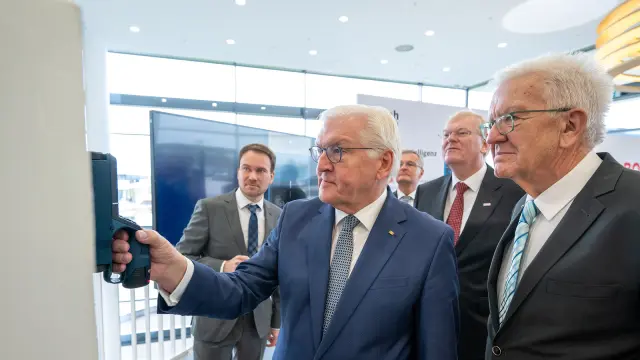 Eine Gruppe von Männern in Anzügen, einer hält ein Gerät gegen eine weiße Oberfläche.