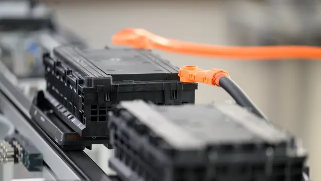 Nahaufnahme von zwei schwarzen Batteriepacks, die durch ein oranges Kabel auf einem Förderband verbunden sind.