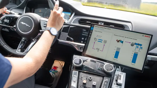Person in einem Auto zeigt auf einen Display mit Fahrdaten und Grafiken.