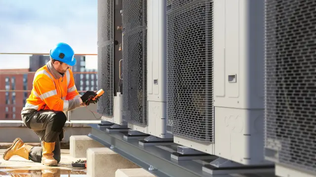 Techniker in Sicherheitsausrüstung überprüft Dach-HVAC-Einheiten mit einem Handgerät.