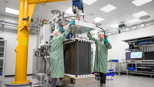 Two workers lifting a large industrial stack with a crane in a production hall.