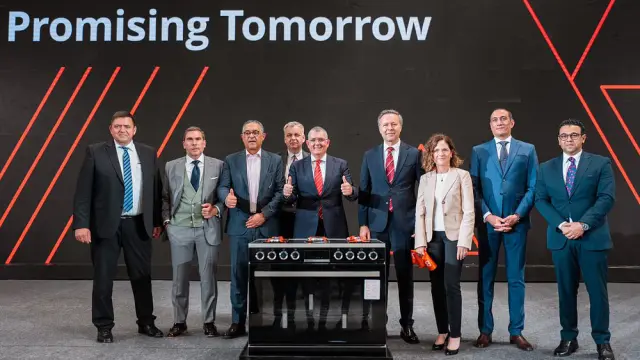  Group of people standing on a stage behind an appliance with “Promising Tomorrow” backdrop.