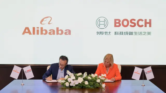 Two people signing documents at a table with Alibaba and Bosch logos behind.