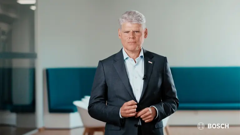 Person in a dark suit stands in a modern interior in front of a turquoise bench. Bosch logo at the bottom right.