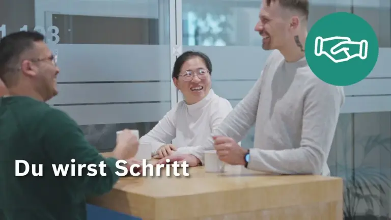 Vier Personen stehen an einem hohen Holztisch in einem modernen Büro, unterhalten sich und lächeln.