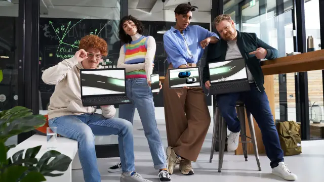 Quatro pessoas, duas mulheres e dois homens, estão com portáteis a exibir imagens de carros contra um quadro negro com equações num escritório moderno.