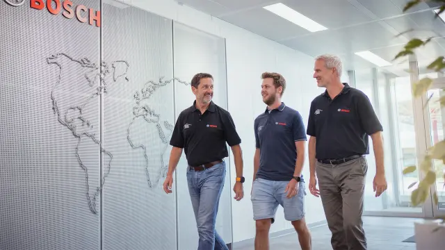 Drei Mitarbeitende gehen durch einen Bosch-Büroflur vor einer Weltkartenwand.