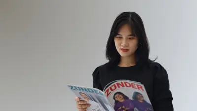 Diem engrossed in reading a magazine titled "ZÜNDER". She can be seen against a black background.