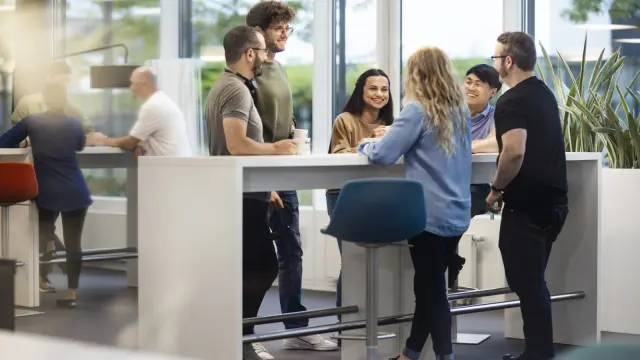 Sechs Personen stehen in einer Büroumgebung an einem Stehtisch.