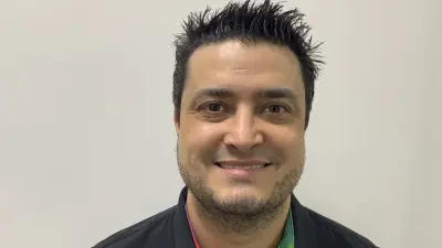 Anderson Gonsalves stands in front of a white wall, wears a polo shirt and smiles into the camera with gelled hair.