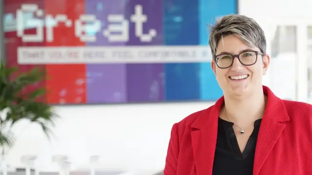 Astrid Hager steht vor einem großen Bild auf dem „Great” steht im Corporate Design von Bosch. Sie trägt einen roten Blazer und lächelt in die Kamera.