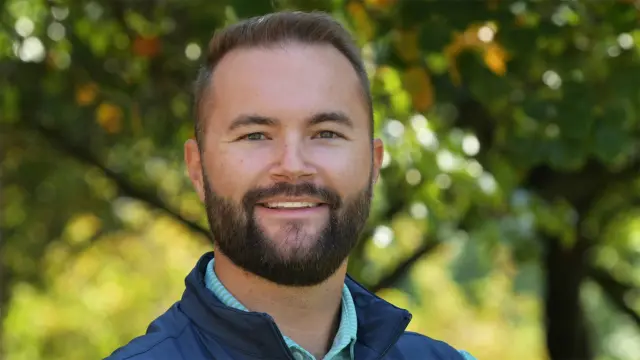 Brad smiles into the camera, trees can be seen blurred in the background.