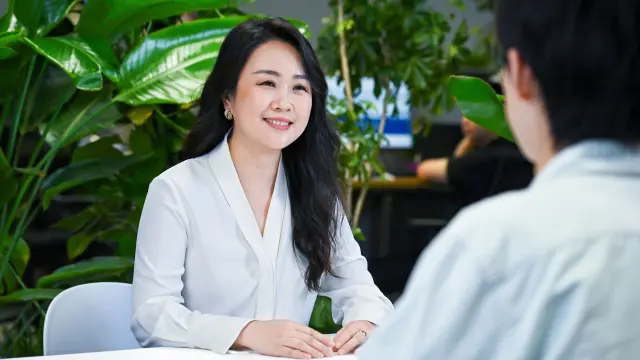 Jessica sitzt gegenüber einer Person und lächelt sie an.