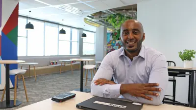 Josef Tsegai, who is sitting at a table with two smartphones and his laptop with the #LikeABosch sticker on it, arms crossed and smiling at the camera.