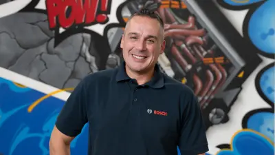 Mario steht vor einer bunten Wand und lächelt in die Kamera.