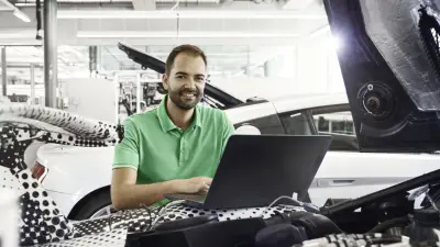 Stefan Bernhardt sitzt zwischen zwei Autos und trägt ein grünes Polo-Shirt. Vor ihm ist ein Laptop, der an ein Auto angeschlossen ist.