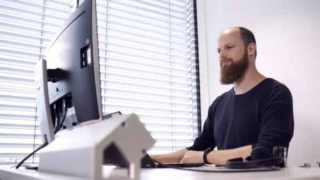 Stefan Essl sitzt an seinem Arbeitsplatz, den Blick auf den Computer-Bildschirm gerichtet. Er arbeitet konzentriert.