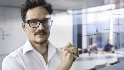 Tobias Pleuger photographed through a pane of glass on which he is writing things with a pen. In the background, two people are sitting at a conference table.
