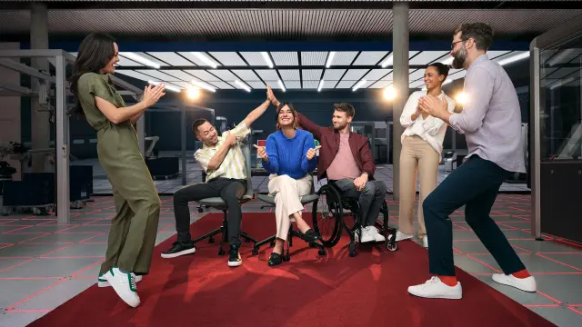 Six people can be seen on a red carpet in a lab. They are all laughing and cheering each other. 
