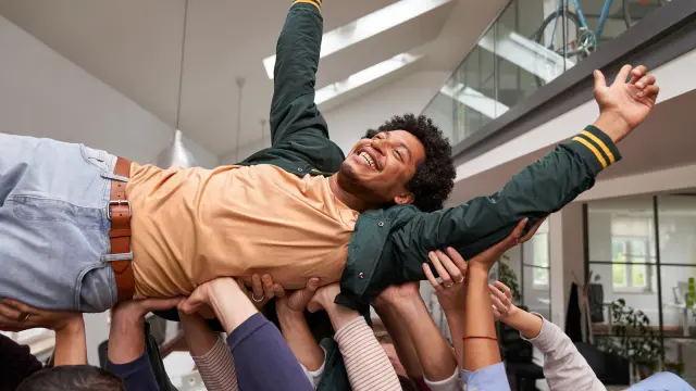 A group of associates are lifting another associate who is celebrated and enjoying it.