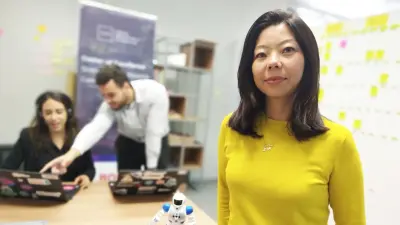 Das Bild zeigt Bosch Mitarbeiterin Flavia. Sie sitzt an einem Tisch vor einem Laptop. Vor ihr steht ein kleiner Roboter. Im Hintergrund ist eine Büroumgebung zu erkennen.