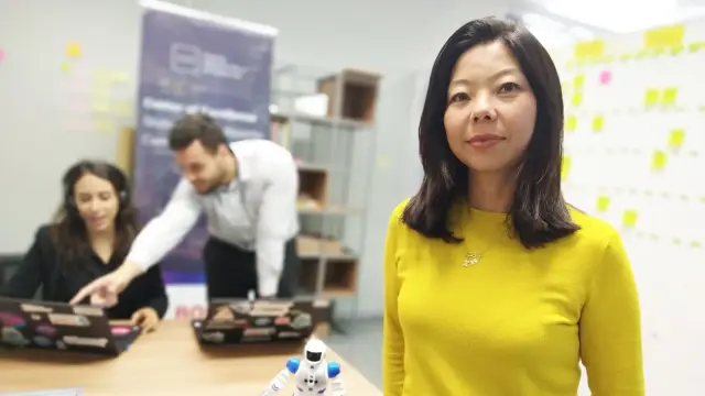 Das Bild zeigt Bosch Mitarbeiterin Flavia. Sie sitzt an einem Tisch vor einem Laptop. Vor ihr steht ein kleiner Roboter. Im Hintergrund ist eine Büroumgebung zu erkennen.