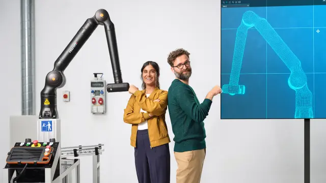 Two people are in a lab, standing between a robot and its digital twin.