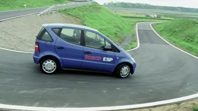 Ein kleines viertüriges blaues Auto in Fahrt auf einen kurvigen Strecke, von der rechten Seite fotografiert