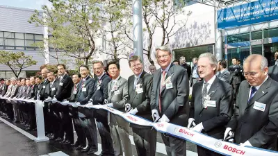 Numerous men in suits next to each other, with gloves and scissors, cutting a long ribbon in front of them