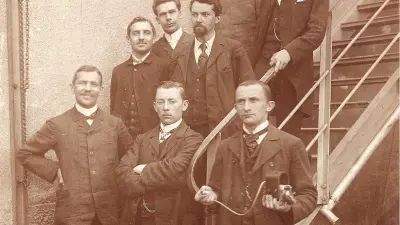 Eight men in suits stand in front of and on a flight of stairs.