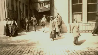 People pass between two buildings to emerge onto a street.