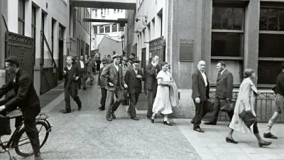 People pass between two buildings to emerge onto a street.