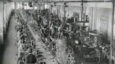 A view of the factory floor from above. Women sit next to each other to the left and right of a long conveyor belt.