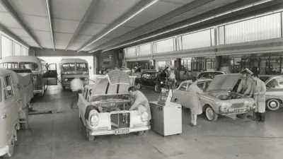In der großen Wagenhalle befinden sich mehrere Busse und Automobile, an denen gerade gearbeitet wird.