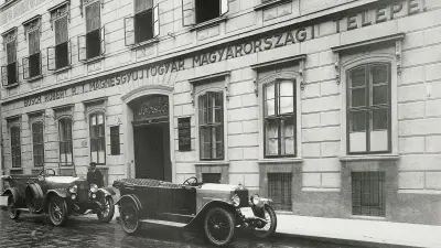 Vor der Hausfront des Budapester Verkaufshauses stehen zwei offene elegante Automobile
