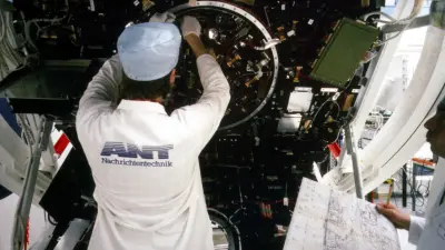 Rückenansicht eines Mannes im weißen Labormantel vor den Innenleben des Satelliten