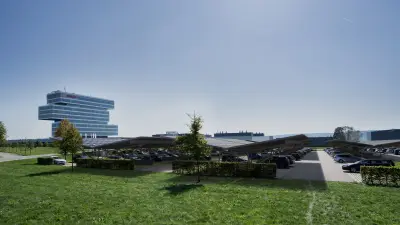 View of a parking lot with roofing made of photovoltaic modules. In the background, the high-rise building of the Renningen research campus.