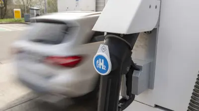 Filling-station pump with a hydrogen symbol. Car (out of focus) passes by.