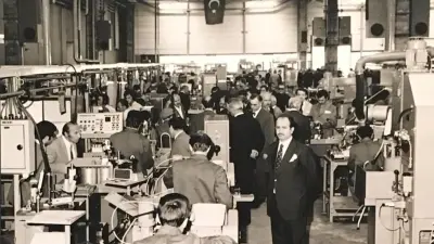 Men at work on a factory floor, watched by other men.