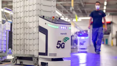 Ein weißer Roboter fährt gestapelte Transportkisten durch eine Werkhalle.