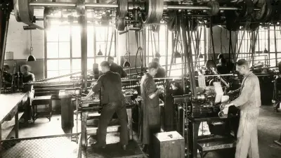 Eine Werkhalle in den 1920er Jahren, in der fünf Männer stehend an Werkbänken arbeiten