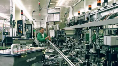 Automatisierte Produktionsstraße, im Hintergrund prüft ein Mann ein Produkt.