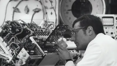 A man in a white coat works on a circuit board