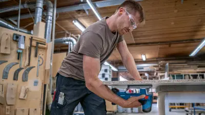 Handwerker in einer Fabrikhalle sägt mit dem Profi-Gerät eine Holzplatte
