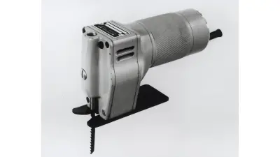 Black and white photo shows the first jigsaw. A small metal plate at the top of the device bears the company name Scintilla.