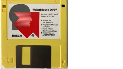 The photo depicts a yellow floppy disk bearing a logo sticker.