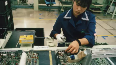 Japanese woman in a blue coat in front of electronic circuit boards