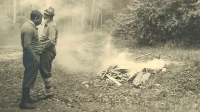 Bosch und Bücher in Jagdkleidung im Wald, im Hintergrund ein Lagerfeuer.