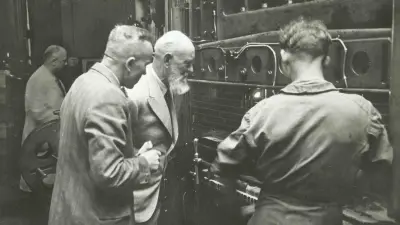 Robert Bosch and two other gentlemen examine a manufacturing machine.