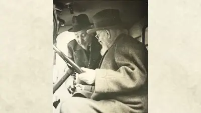 Robert Bosch in the driver's cab of a truck, sitting at the wheel, Max Rall leans toward him.